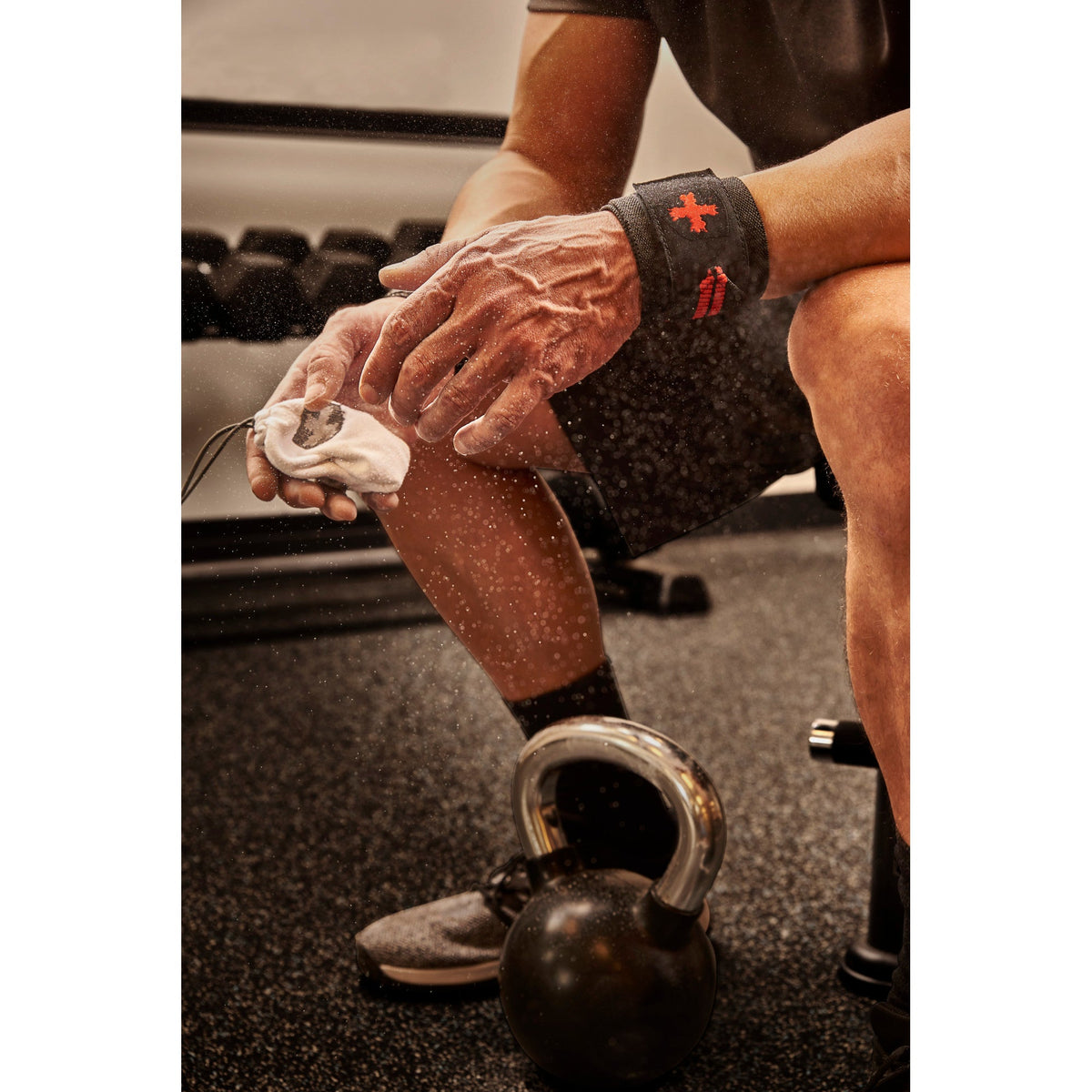Hands squeezing Harbinger chalk ball with dust cloud, kettlebell on gym floor